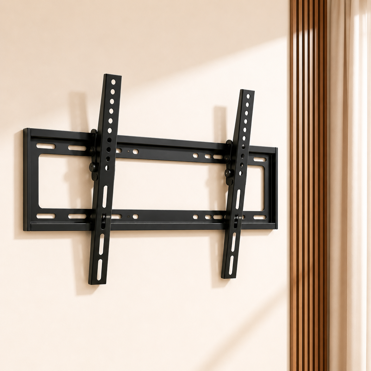 A black metal flat-screen TV wall mount bracket mounted on a beige wall, shown with the arms extended. The background features warm sunlight and vertical wood slats on the right side.